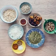 Ingredienser till granola; havregryn, frön, nötter, aprikos, russin och kryddor på assietter och i små skålar.