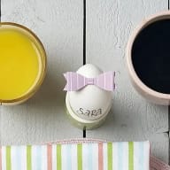 En frukostbricka med ett glas juice, en kopp kaffe och ett ägg med en rosett på.