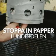 Fingrar fyller ett tändrör med tidningspapper.