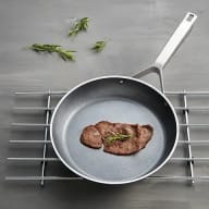 En stekpanna med en köttbit står på ett grillgaller med några örtkvistar bredvid.