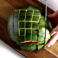 En person skär ett mönster i en vattenmelon på en skärbräda.
