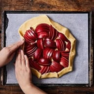 En person förbereder en paj med skivad frukt på en bakplåt.