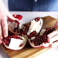 En person öppnar ett granatäpple på en skärbräda och visar de röda kärnorna inuti.