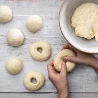 En person formar degbitar på ett träbord bredvid en skål med mer deg.