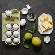 En bricka med ägg, smör, limefrukter, kryddor och salt på en mörk yta.