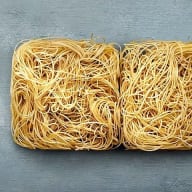 Två rektangulära behållare fyllda med tunna spaghettiliknande nudlar står på en yta.