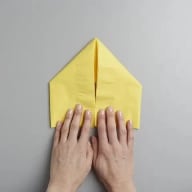 En person viker ett pappersflygplan av ett gult papper på en ljus yta.