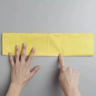 En person håller och pekar på en rektangulär papperslapp på en slät yta.