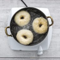 En kastrull med tre bagels flyter i vatten på en elektrisk kokplatta.