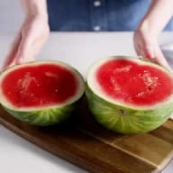En person håller en delad vattenmelon på en skärbräda.