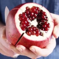 En person håller en delad granatäpple i handen.