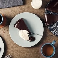 En tallrik med en bit tårta och grädde står på ett bord bredvid kaffekoppar.