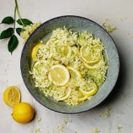 En skål med citronskivor och blommor står bredvid en hel citron på ett bord.