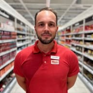 En person med skägg står i en butiksgång med hyllor fyllda av varor.