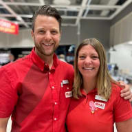 Två personer i likadana skjortor står bredvid varandra i ett rum med synligt tak.