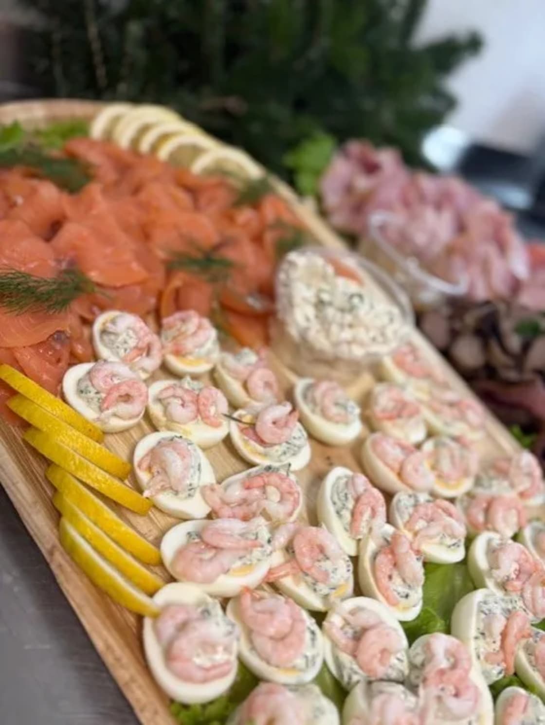 Serveringsfat med ägghalvor toppade med räkor, omgivna av skivad lax, citron och en skaldjurssallad.