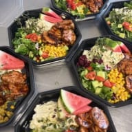 Flera matlådor med grillad kyckling, sallad, majs och melonskivor.