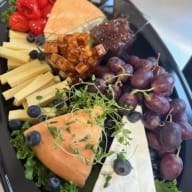 Ostbricka med flera ostar, vindruvor, bär, marmelad och färska örter.