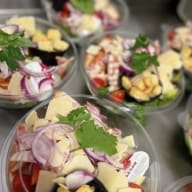 Flera salladsskålar med caesarsallad toppade med ost, lökringar, krutonger och en liten dressingbehållare.