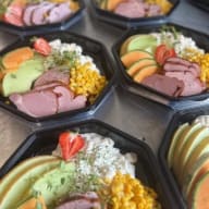 Flera matlådor med skivat kallskuret, majs, melon och potatissallad.