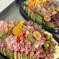 Stort serveringsfat med konstfullt upplagda charkuterier och färsk frukt.