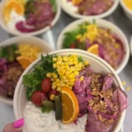 En skål med sallad, majs, skivad rostbiff, krämig sås och en apelsinskiva hålls av en hand.