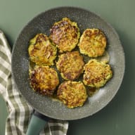 En stekpanna med sju zucchinifrotters står på ett underlag bredvid en vikt handduk.