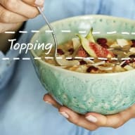 En person håller en skål med frukost och tillsätter topping med en sked.