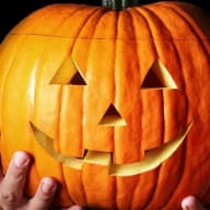 En person håller en halloweenpumpa med triangelformade ögon och en leende mun.