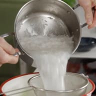En person häller ris från en kastrull genom en sil över en skål.