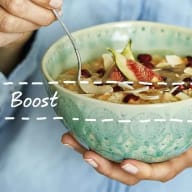 En person håller en skål med frukost innehållande fikon och nötter medan en sked förs mot skålen.