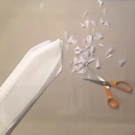 Ett pappersflygplan flyger mot en sax som klipper sönder papper.