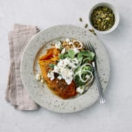 Hasselbacksbackad pumpa ligger på en tallrik med marinerad fetaost, machesallad och nötter.