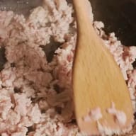 En träslev rör i köttfärs i en kastrull.