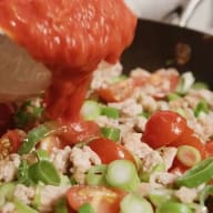 En person häller sås över en sallad med kött, tomater och grönsaker.