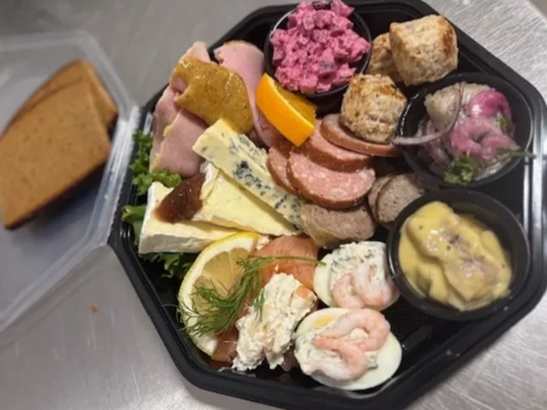 Plockbricka med olika ostar, kallskuret, räkor, ägghalvor och bröd.