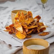 En hög med chips ligger på en servett bredvid två skålar på en vit duk.