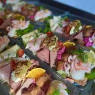 Brickor med öppna smörgåsar toppade med skivat kött, räkor och olika pålägg.