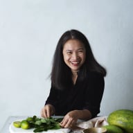 En person ler vid ett bord med olika matvaror som grönsaker, frukter och skålar.