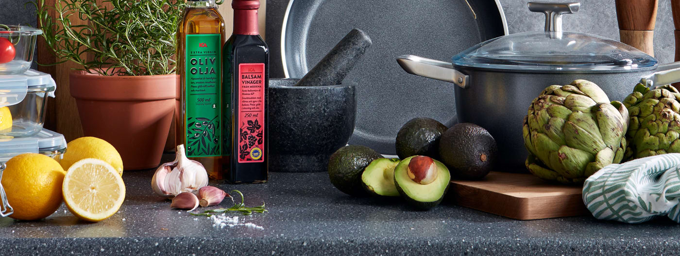 En flaska olivolja och en flaska balsamvinäger på en köksbänk med citron, vitlök och rosamarin.