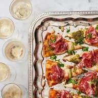 Pizzabitar med salami, sparris, pesto och mozzarella på ett silverfat. Glas med kolsyrad dryck bredvid