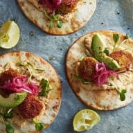 Falafel, avokadoskivor, syrad rödlök på tortillabröd. Pressad limeskiva bredvid