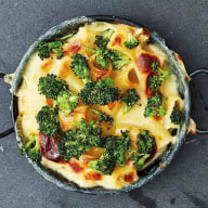 En gryta med broccoli och ost serveras i en stekpanna på en mörk yta.