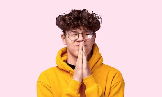 En person med glasögon har slutna ögon och pressar ihop sina händer.