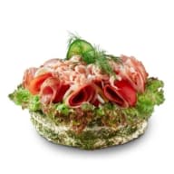 Rund smörgåstårta toppad med sallad, räkor, skivade charkuterier och dill.