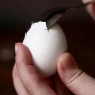 En person håller ett ägg och skalar det med en kniv.