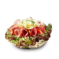 Rund smörgåstårta garnerad med hoprullade pålägg och salladsblad.