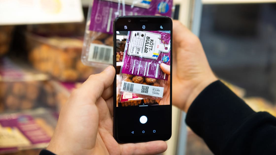 En hand håller en mobil och scannar en förpackning köttbullar med kameran.