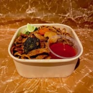 Takeawaylåda med wokade nudlar, grönsaker, limeklyftor och en liten såsbehållare.