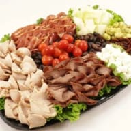 svart serveringsfat fullt med olika kallskurna köttsorter dekorerat med sallad och frukt